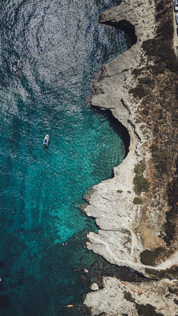 Drohnenbild einer dramatischen Felsenküste auf Zakynthos mit glasklarem, blaugrünem Wasser und einem Boot im Bild