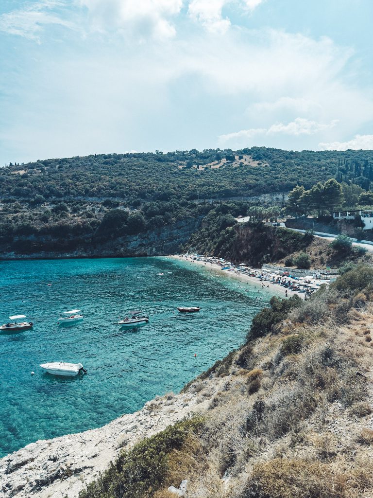 Foto vom Strand Makris Gialos auf Zakynthos mit Booten im Wasser und grünen Hügeln im Hintergrund, aufgenommen vom Felsvorsprung