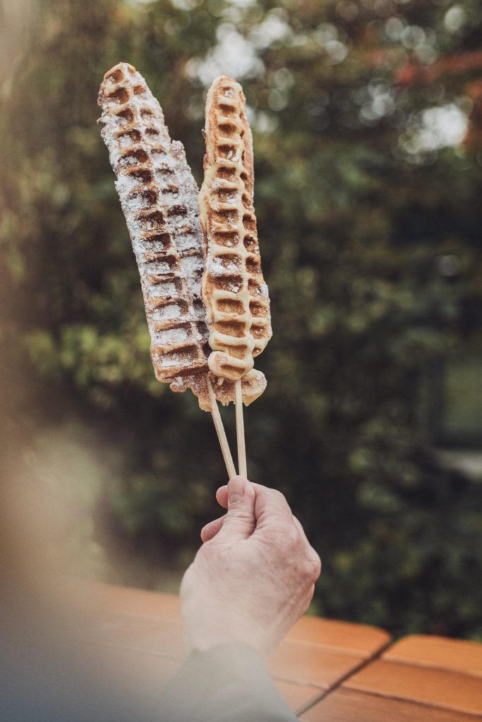 Zwei Waffeln am Stiel mit Puderzucker, gehalten von einer Hand auf dem Kürbisfest in Deutschland