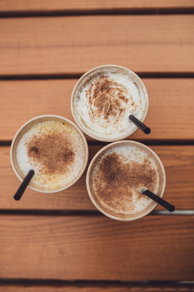 Drei Pumpkin Spice Lattes mit Sahne und Zimt auf einem Holztisch beim Kürbisfest in Deutschland