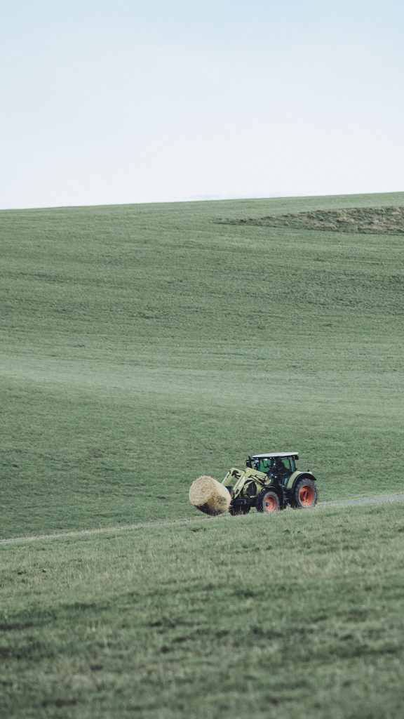 Ein Traktor transportiert eine große Heuballe über die grünen Hügel des Sauerlands. Landwirtschaftliche Arbeiten aus nächster Nähe erleben – so fühlt sich das Campen auf dem Bauernhof am Hennesee an: ursprünglich, echt und entschleunigend.