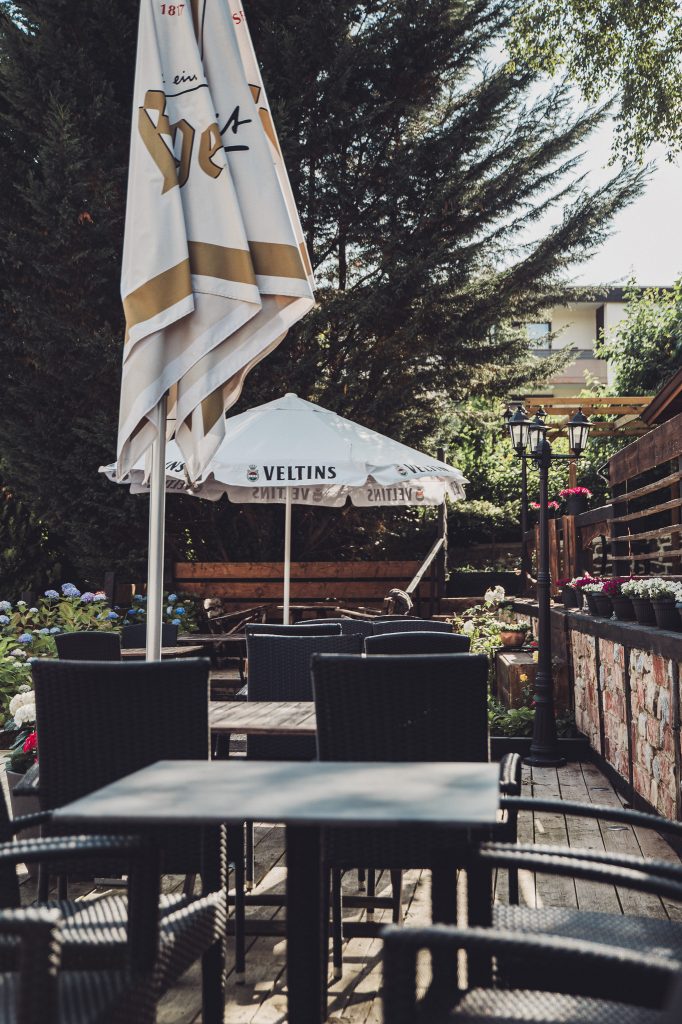 Terrasse mit dunklen Rattanstühlen und Veltins-Sonnenschirmen im Café Mona & Lisa in Horn-Bad Meinberg