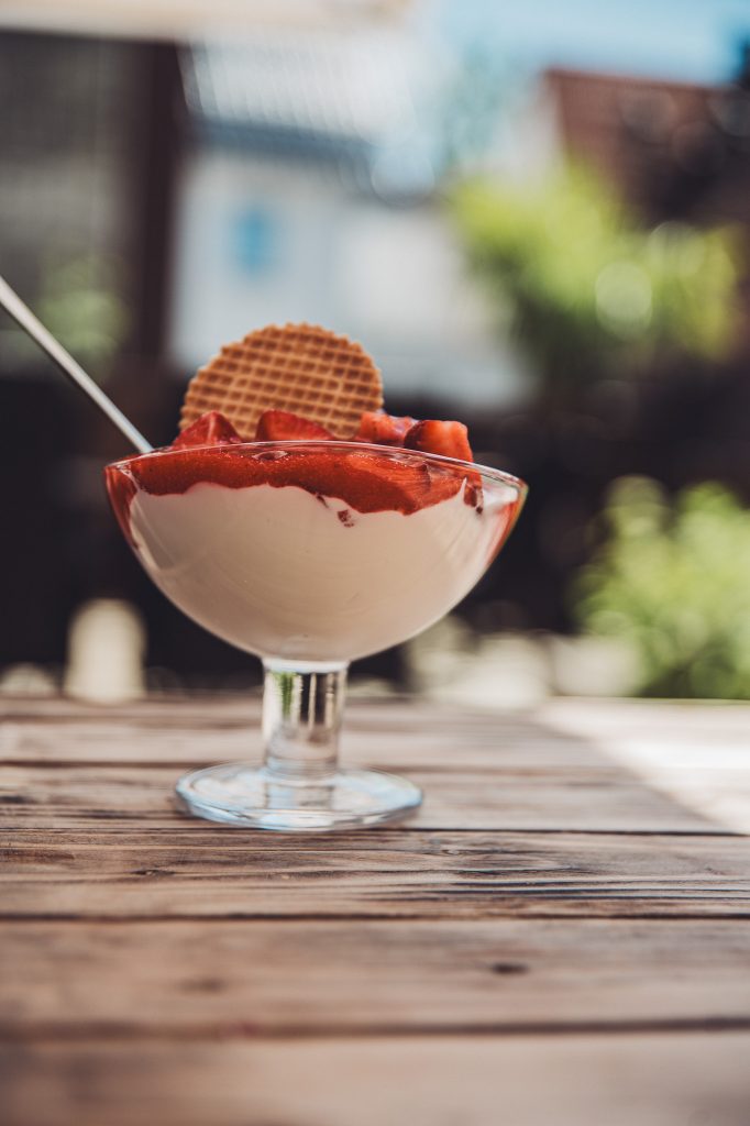 Glas mit Joghurt-Eis, frischen Erdbeeren und Waffel auf Holztisch in der Sonne vor dem Café Mona & Lisa