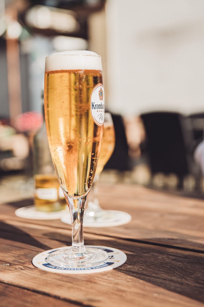 Nahaufnahme eines Krombacher Pils auf Holzuntersetzer bei Sonnenschein im Café Mona & Lisa