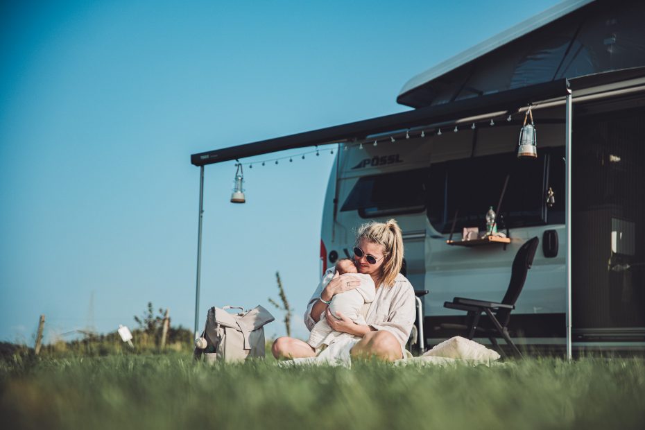Mutter sitzt vor Camper und hält ihr Baby im Arm