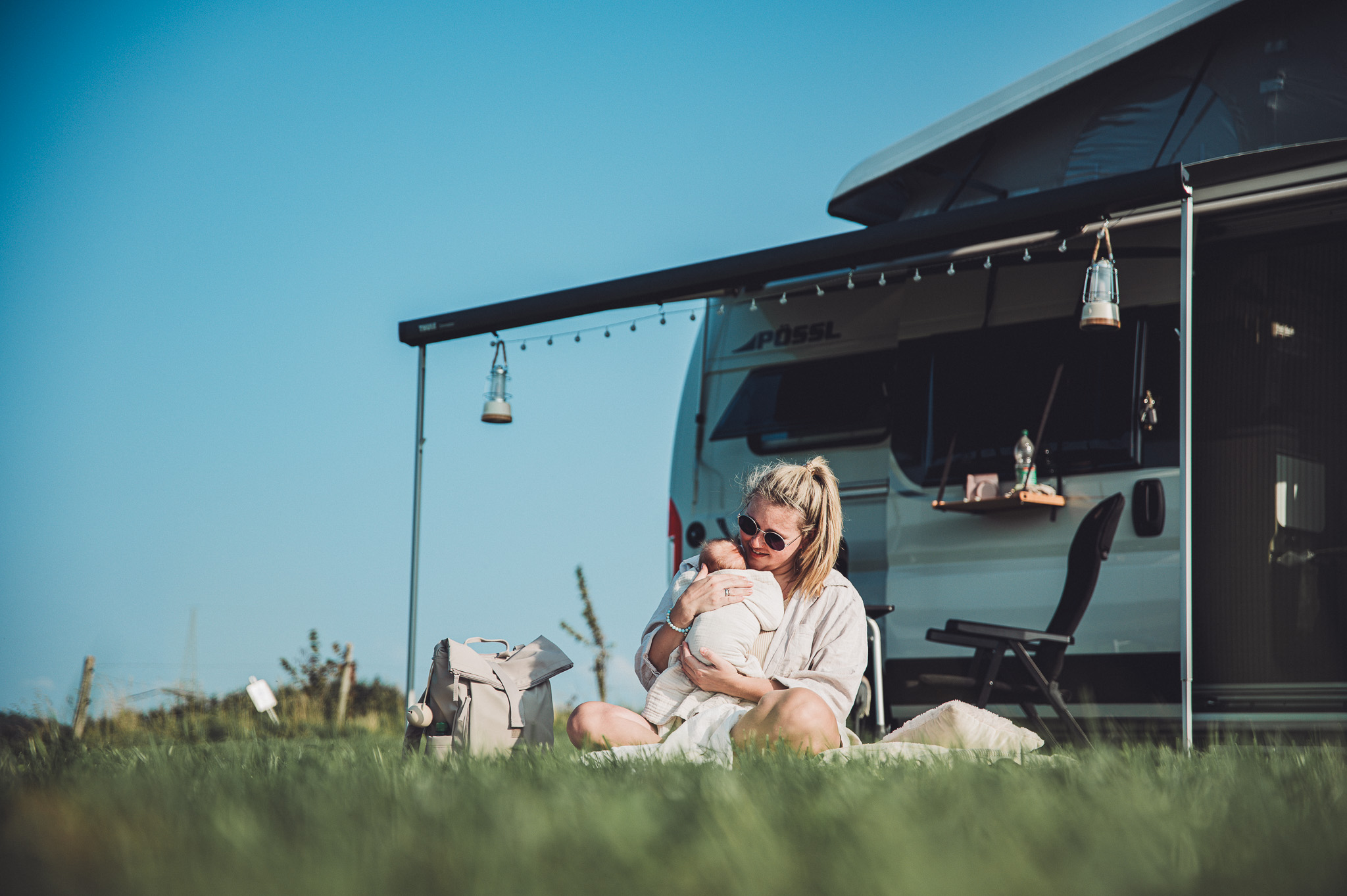 Mutter sitzt vor Camper und hält ihr Baby im Arm