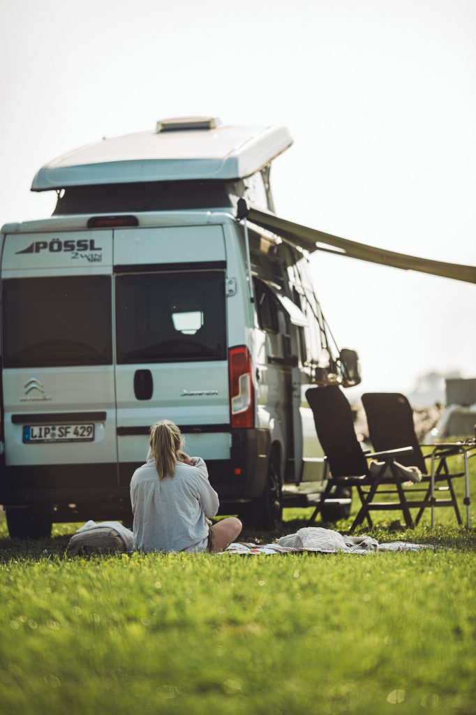 Frau mit Baby sitzt hinter dem Camper mit Campingstühlen