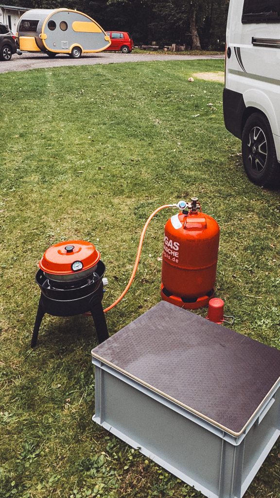 Gaskocher mit roter Gasflasche und Omnia-Backofen auf einer Parzelle am Campingplatz Niemetal.