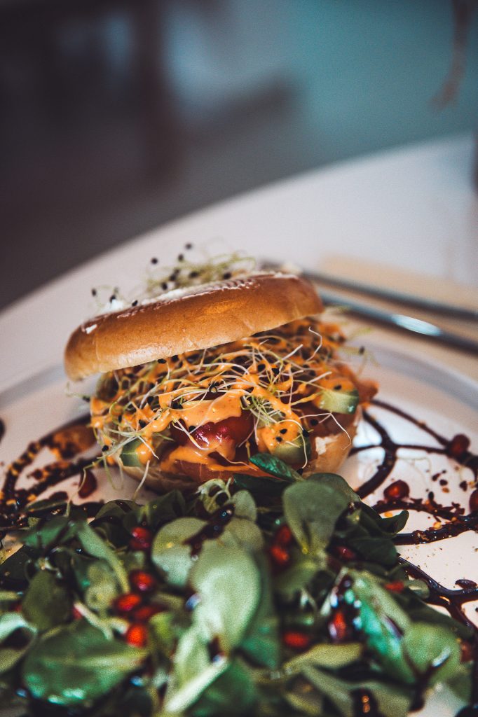 Bagel mit frischem Salat, Sprossen und Dressing im Betty’s Café Wittlich, serviert mit grünem Beilagensalat.