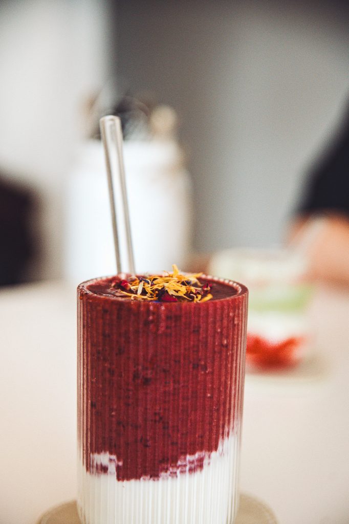 Beeriger Smoothie mit Joghurt und Blüten-Topping im Betty’s Café Wittlich auf hellem Tisch serviert.