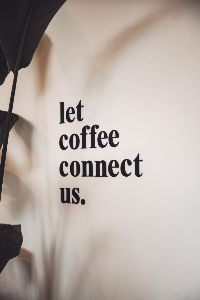 Schriftzug „Let coffee connect us“ an der Wand im Betty’s Café Wittlich, eingerahmt von Pflanzen und weichem Licht.