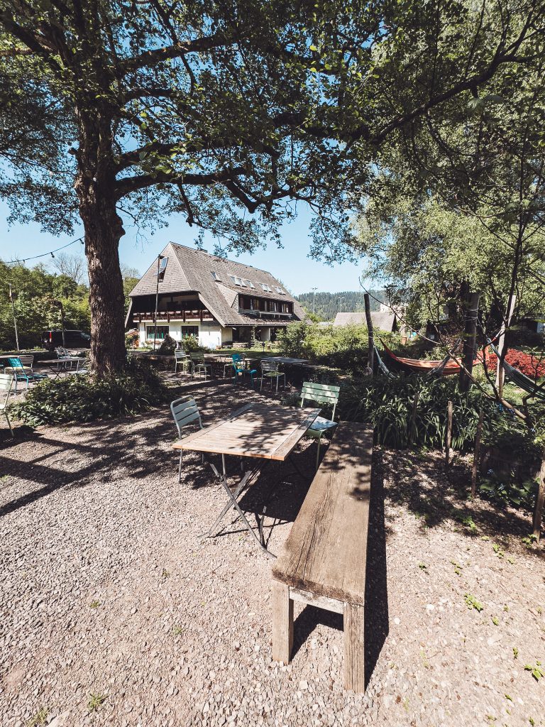 Bistro-Terrasse mit Holztisch und Stühlen unter Bäumen auf dem Camping Möslepark Freiburg