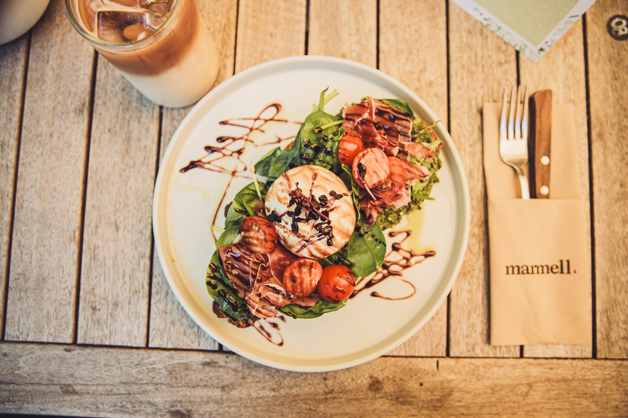 Teller mit Burrata-Toast, Basilikum, Schinken und Tomaten auf Holztisch im Café Marmell Freiburg.