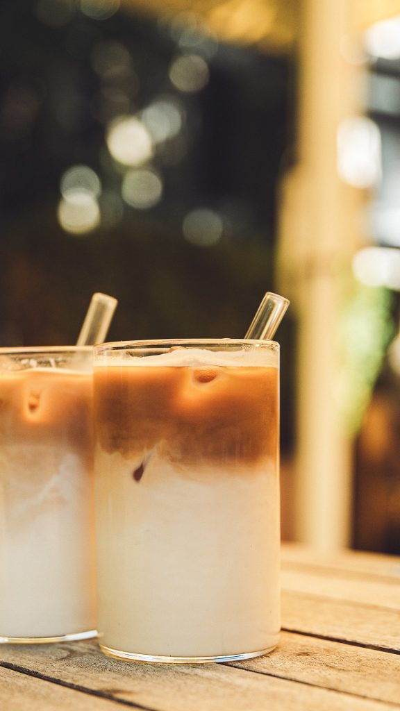 Zwei Gläser Iced Latte mit Glasstrohhalm auf einem Holztisch im Café Marmell Freiburg.