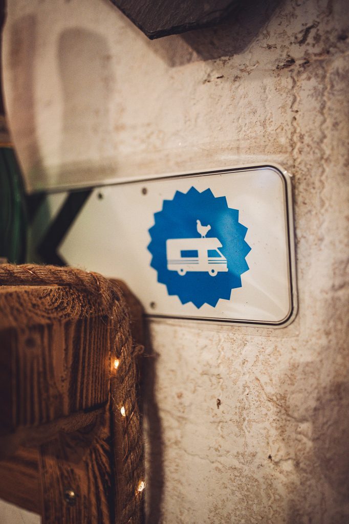 Weiß-blaues Landvergnügen-Schild mit Camper-Symbol an der Wand im Hofladen von Kochs Hof