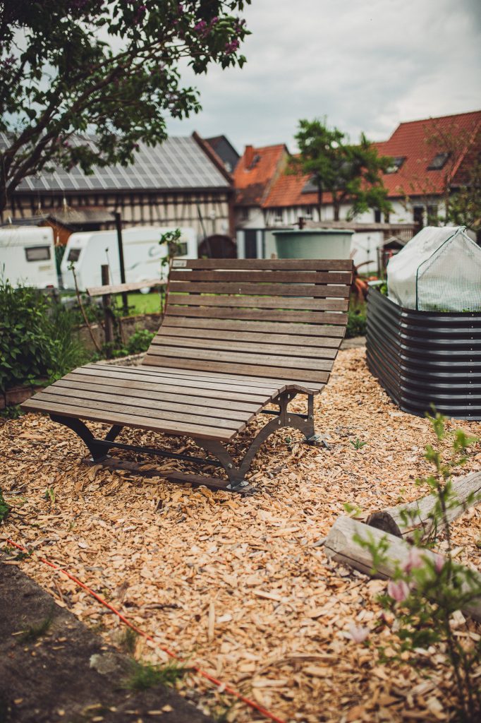 Holzliegebank im Garten von Kochs Hof mit Blick auf Wohngebäude und Camper