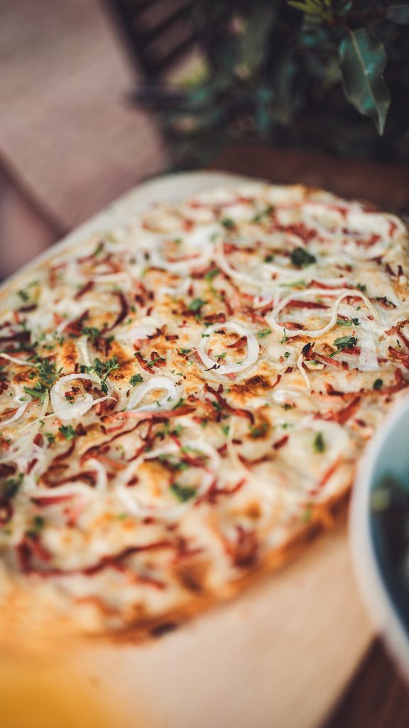 Knuspriger Flammkuchen mit Zwiebeln und Schinken auf Holzbrett