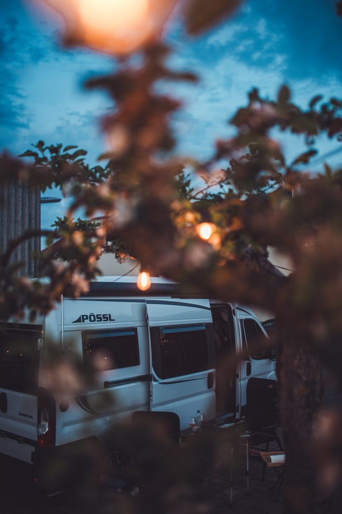 Camper am Weingut Holzwarth in der Abenddämmerung, eingerahmt von einer Lichterkette zwischen den Bäumen.
