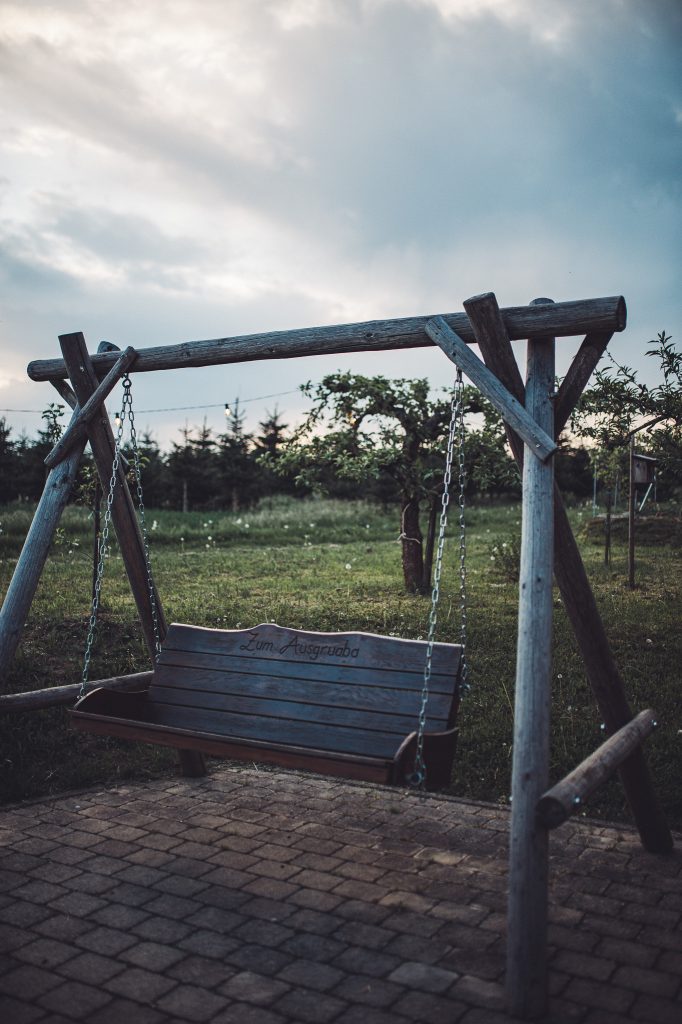 Holzschaukel mit der Aufschrift Zum Ausgruaba auf gepflastertem Platz im Abendlicht am Weingut Holzwarth.