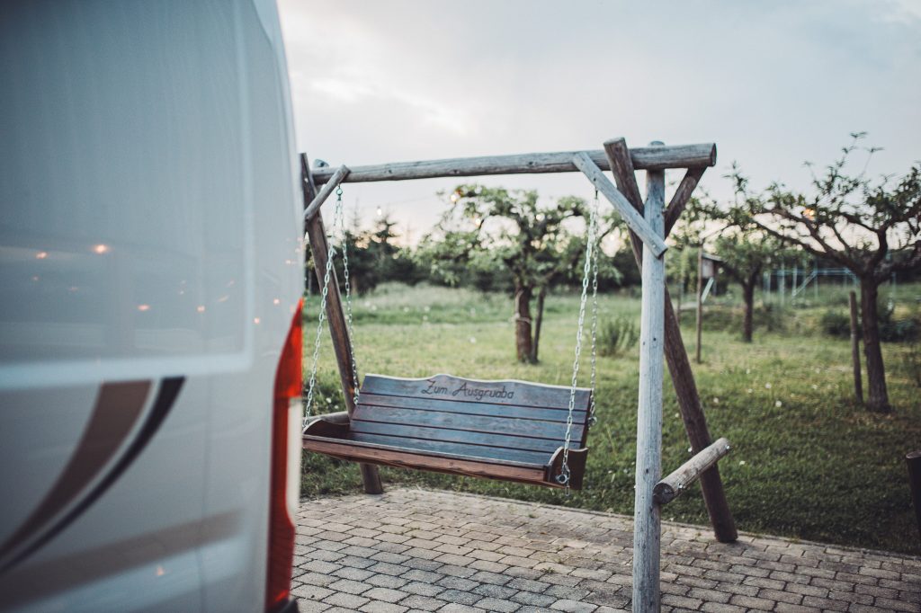 Camper neben einer Holzschaukel auf dem Hof des Weinguts Holzwarth in der Abendstimmung.