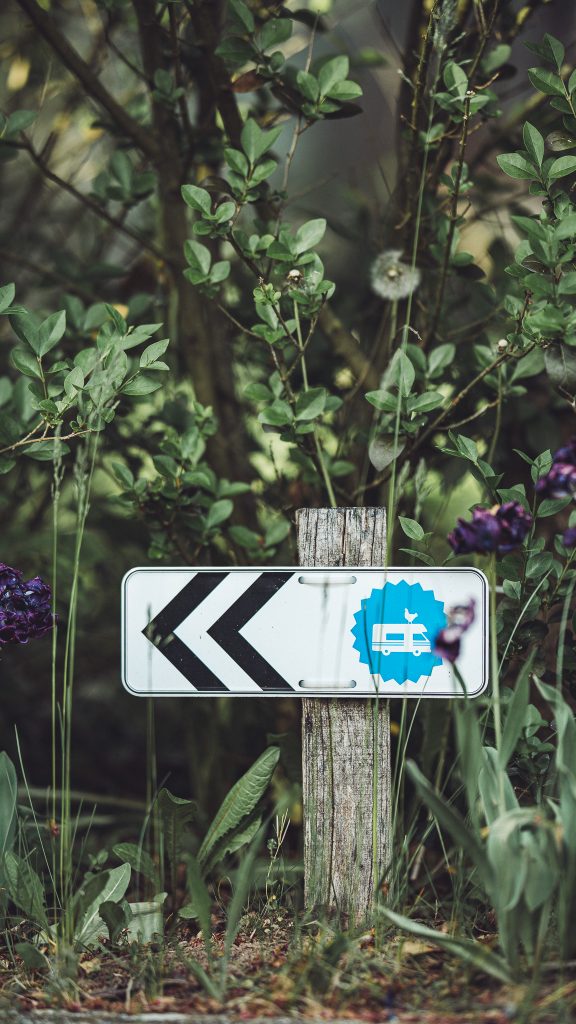 Kleines Richtungsschild mit Landvergnügen-Symbol zwischen grünen Sträuchern auf dem Gelände des Weinguts Holzwarth.