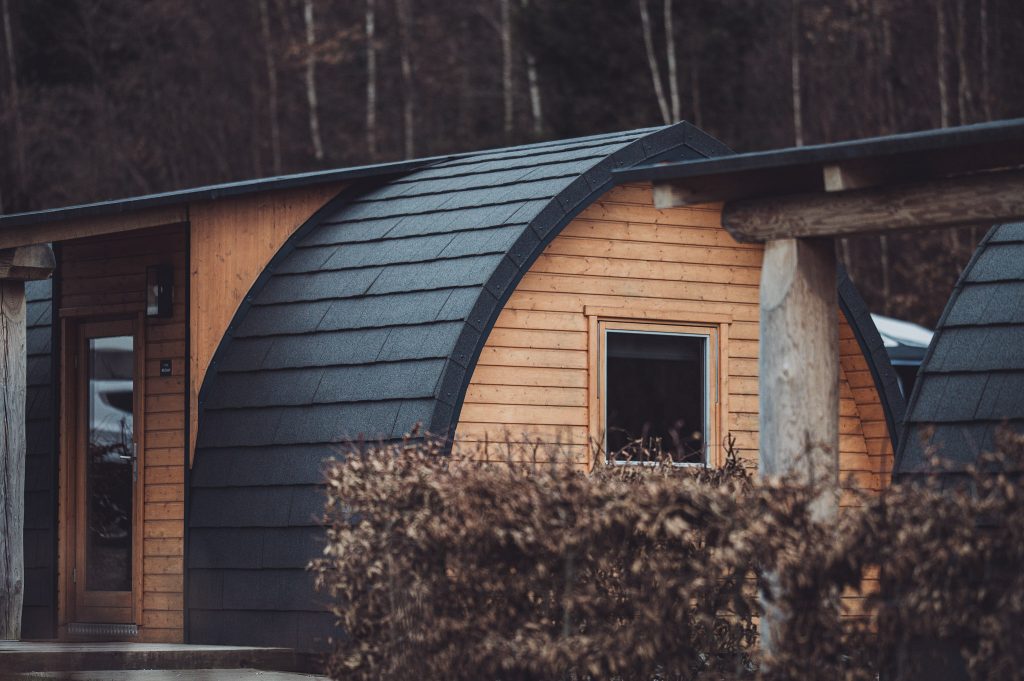 Holzpod im Harz Camp Goslar mit gebogenem Dach und Holzfassade vor winterlich kahlem Wald und Hecken im Vordergrund