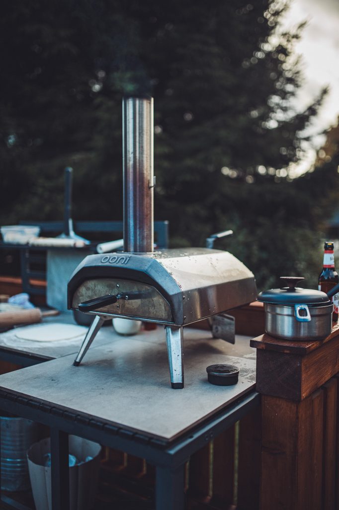 Ooni Pizzaofen mit leichtem Rauch auf einer Outdoor Kochstation mit Topf und Bierflasche daneben im Harz