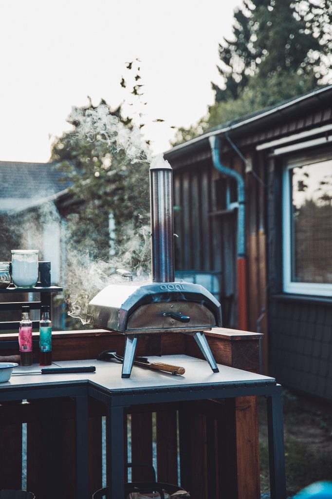 Silberner Ooni Pizzaofen mit Rauch auf einer Outdoor Arbeitsfläche auf dem Campingplatz im Harz