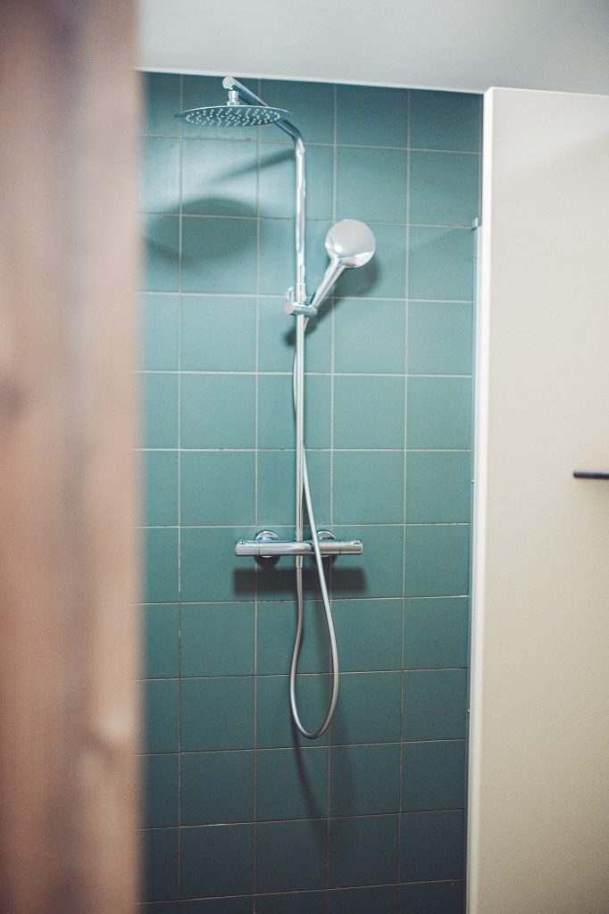 Moderne Regendusche mit grünen Fliesen und Handbrause im Sanitärbereich des Campingplatzes im Harz