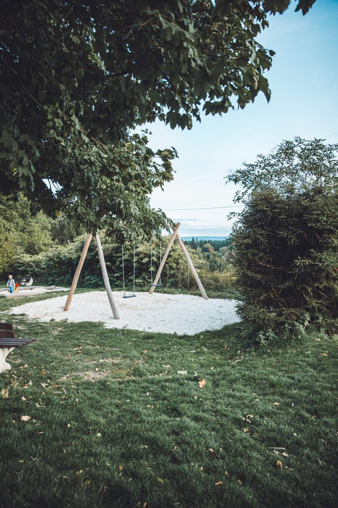 Spielplatz mit Holzschaukel und Sandfläche auf einer Wiese mit weiter Aussicht über Wälder im Harz