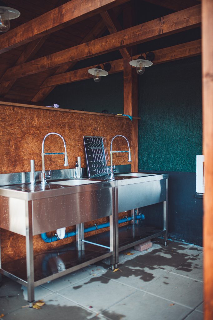 Überdachter Spülbereich mit zwei Edelstahlspülbecken und modernen Wasserhähnen auf dem Campingplatz im Harz