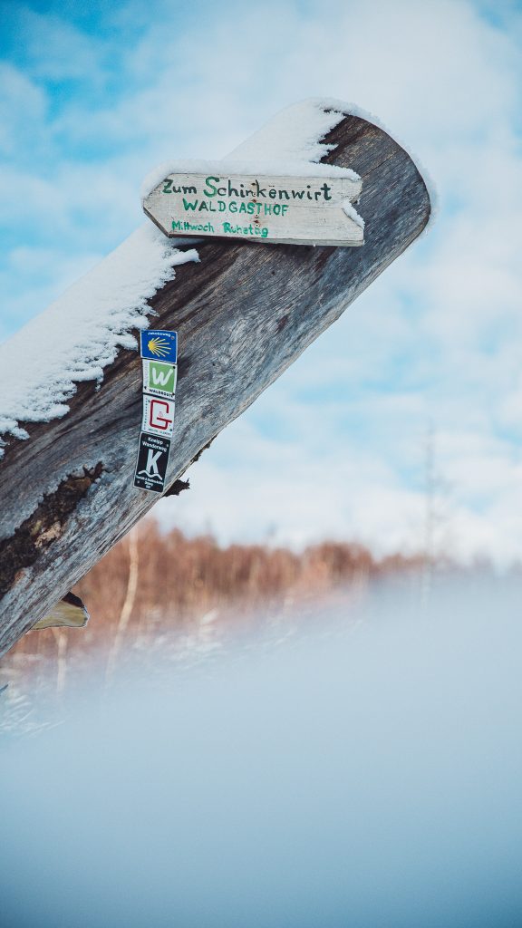 Verschneiter Holzwegweiser mit Aufschrift Zum Schinkenwirt Waldgasthof
