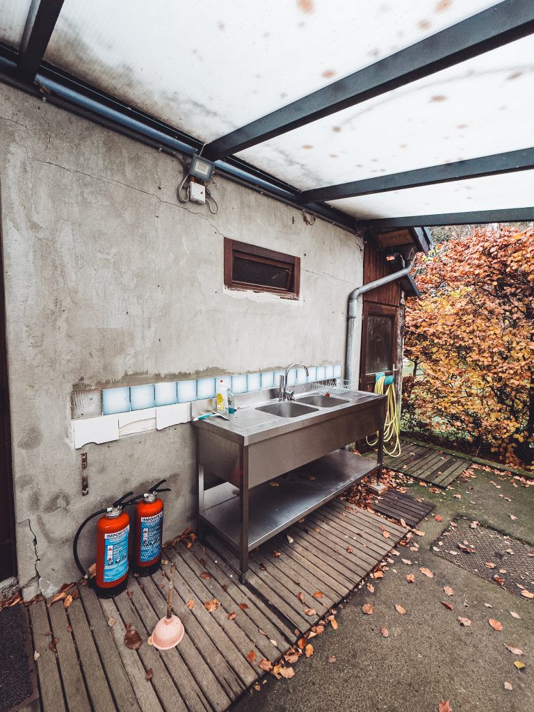 Überdachte Geschirrspülstation mit Doppelspüle am Camping des Charmilles in Belgien, Herbstlaub und nasser Boden