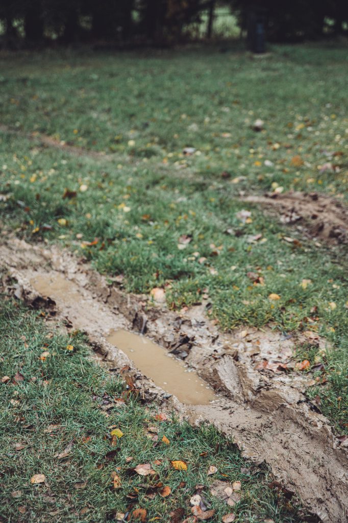 Matschige Fahrspur mit Wasserpfütze auf lehmigem Stellplatz am Camping des Charmilles in Belgien, Herbstlaub auf der Wiese