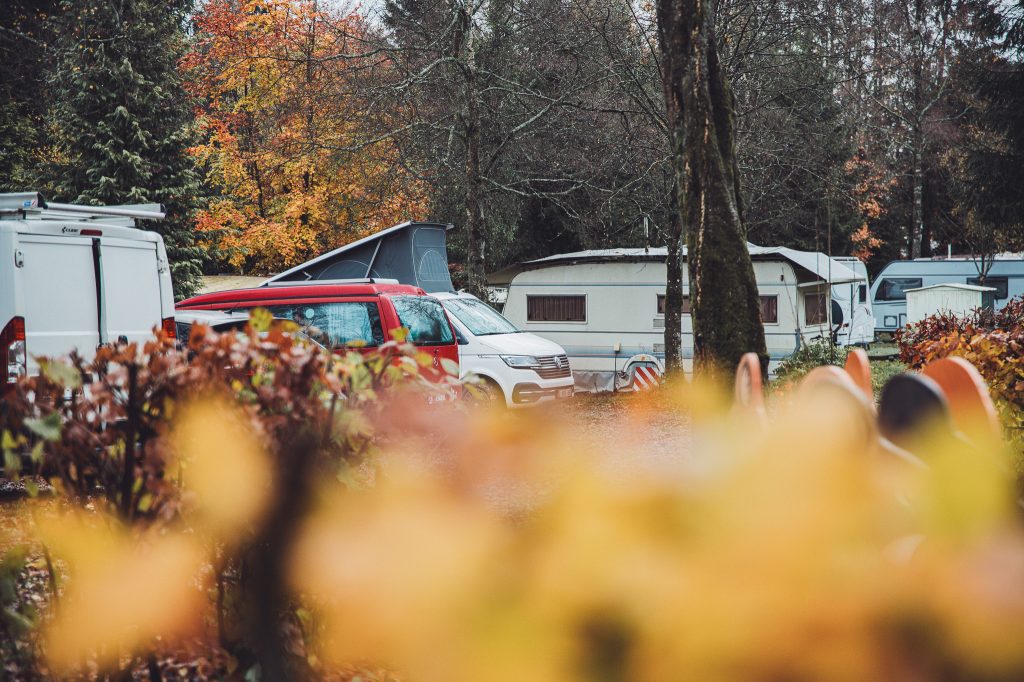 Wohnmobile und Wohnwagen auf ruhigem Stellplatz zwischen bunten Herbstbäumen am Camping des Charmilles in Belgien