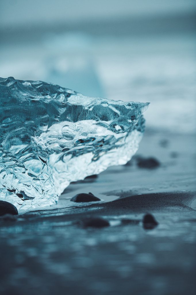 Transparenter Eisblock liegt auf schwarzem Sand am Diamond Beach in Island