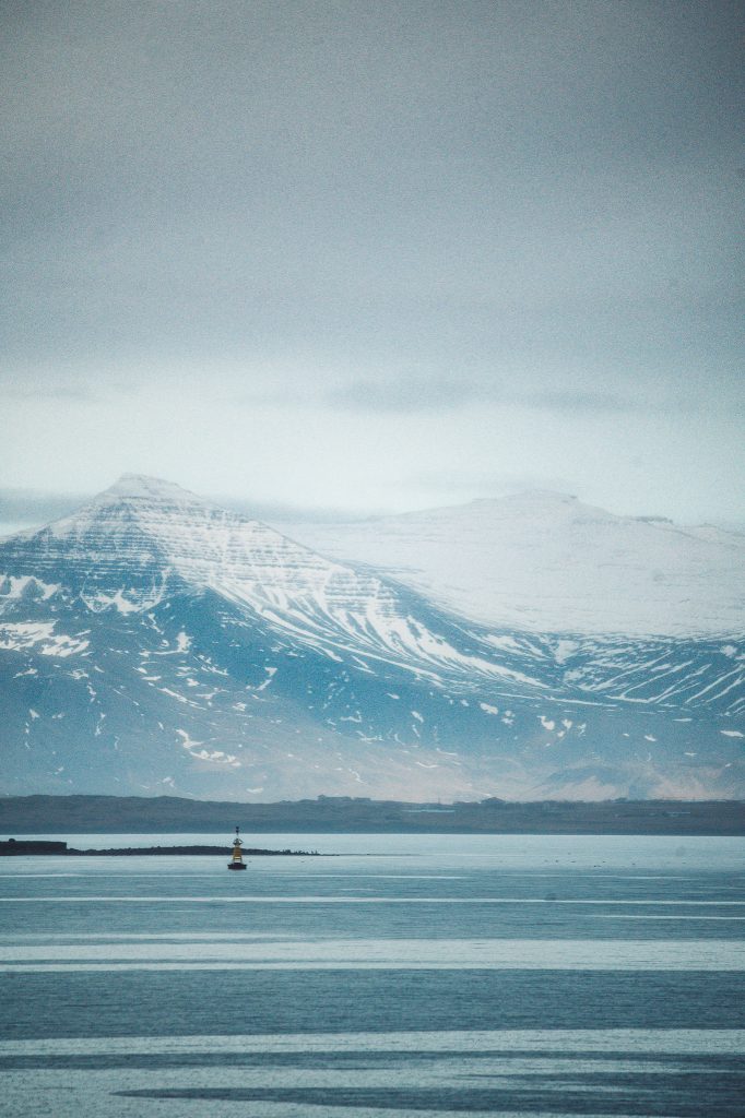 Fjord mit ruhigem Wasser und schneebedeckten Bergen im Nebel in Island