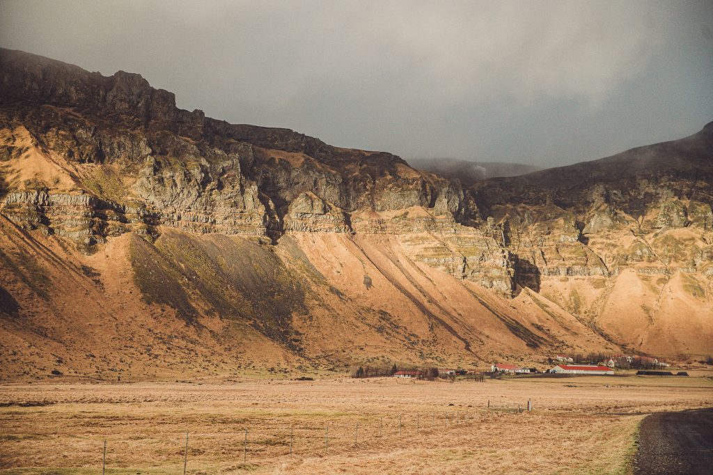 Isländische Häuser am Fuß hoher Felswände in weiter karger Landschaft