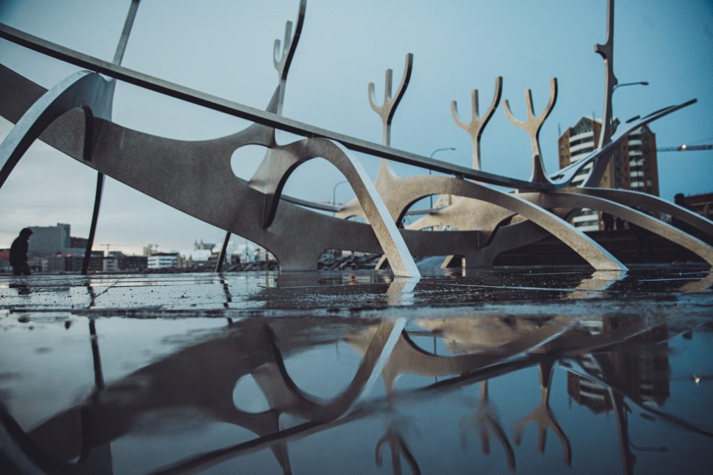 Sólfar Skulptur in Reykjavík mit Spiegelung im nassen Boden und Stadt im Hintergrund