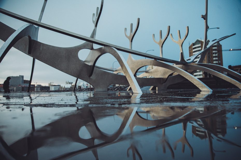 Sólfar Skulptur in Reykjavík mit Spiegelung im nassen Boden und Stadt im Hintergrund