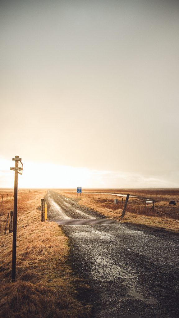 Schotterstraße in flacher Landschaft mit Verkehrsschild und weitem Horizont in Island