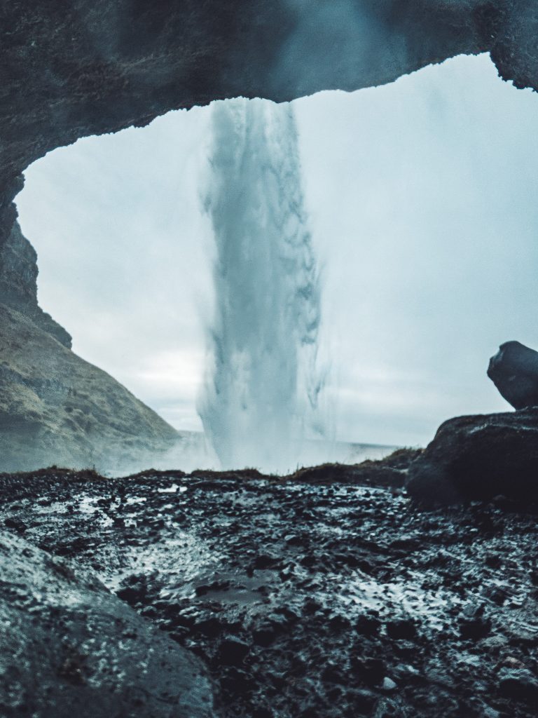 Wasserfall Seljalandsfoss durch eine dunkle Felsöffnung fotografiert mit nassem Boden im Vordergrund