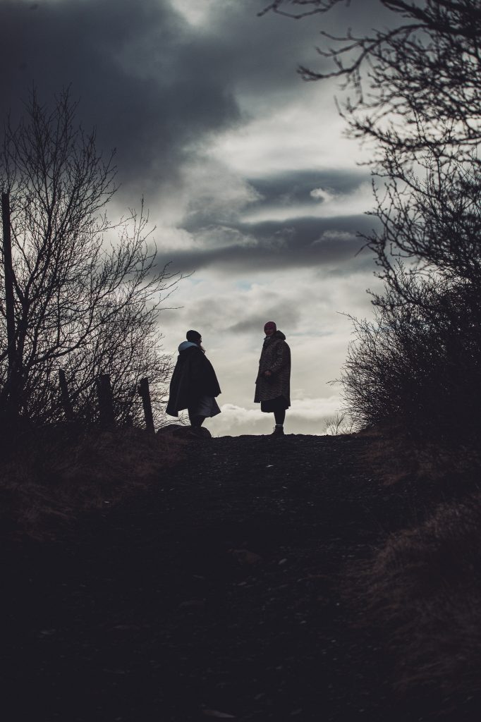 Zwei Personen als Silhouetten auf einem Hügel vor dramatischem Himmel in Island