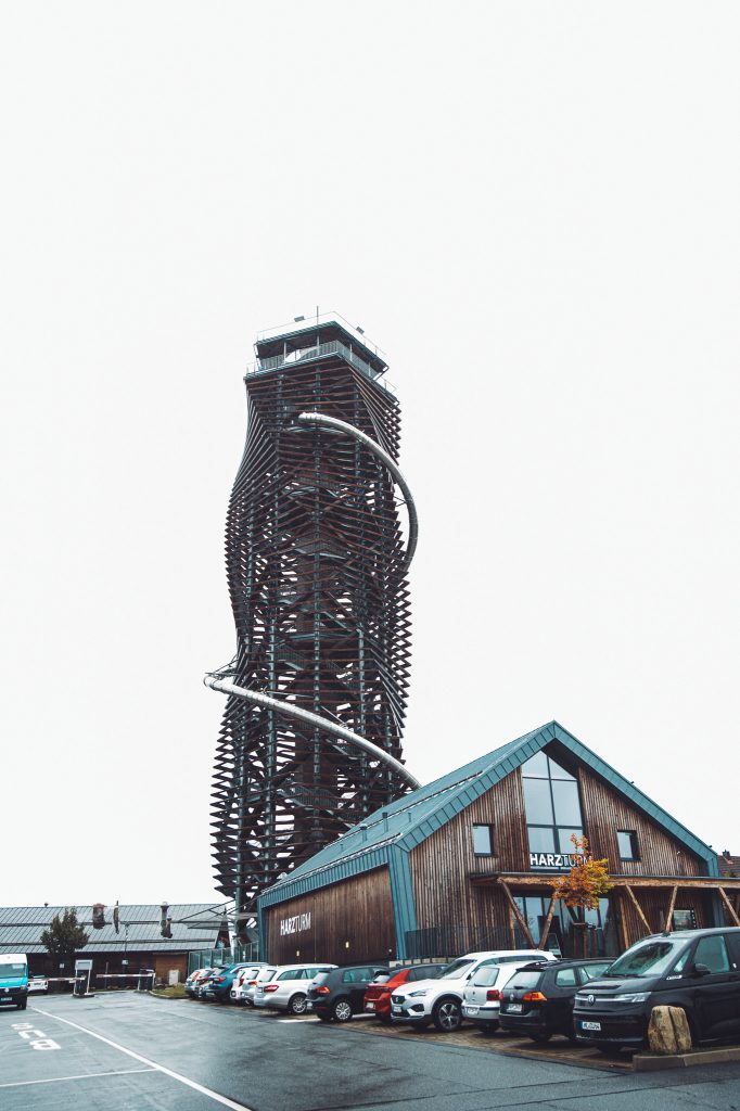 Hoher Harzturm in Torfhaus mit Rutsche und angrenzendem Gebäude des Nationalparkzentrums sowie geparkten Autos an einem regnerischen Tag