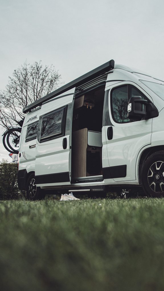 Nahaufnahme eines weißen Campervans mit offener Schiebetür auf dem Stellplatz am Campingplatz Großes Meer