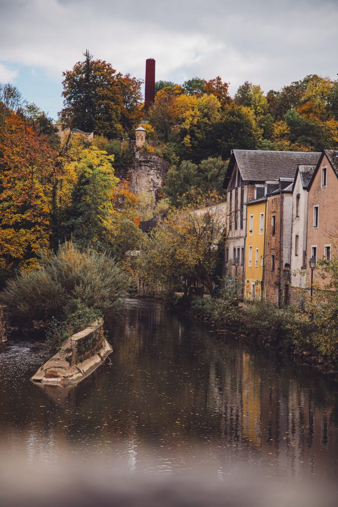 Ruhiger Flusskanal im Luxemburger Grund mit Häuserzeile, Bäumen in Herbstfarben und bewölktem Himmel
