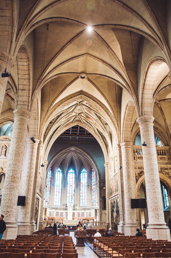 Innenraum einer Kirche in Luxemburg Stadt mit hohen Gewölben, Säulen, Sitzbänken und bunten Glasfenstern