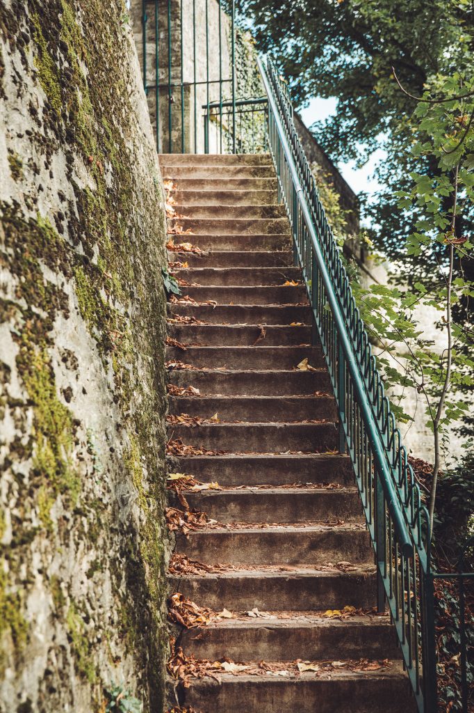Steile Steintreppe mit grünem Geländer an moosiger Mauer, Herbstlaub auf den Stufen, Luxemburg Stadt