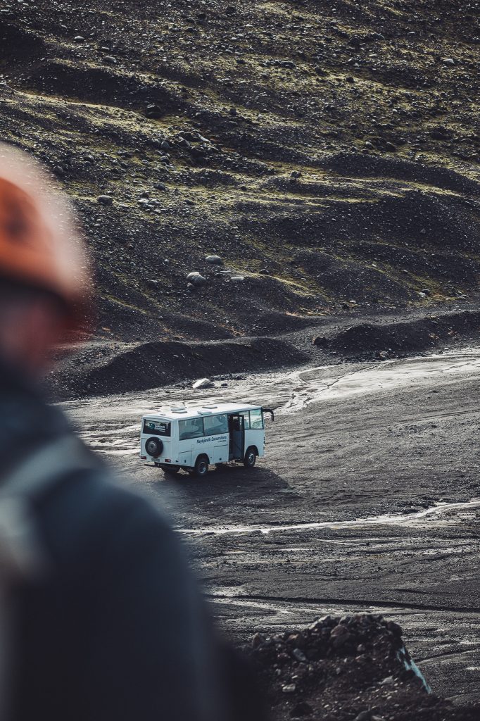 Ein weißer Geländebus fährt durch eine graue, karge Vulkanlandschaft am Fuße des Gletschers.