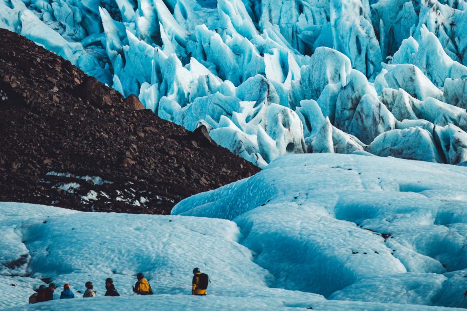 Fernaufnahme einer Wandergruppe auf einer weiten Eisfläche vor einem Hintergrund aus spitzen Eistürmen.